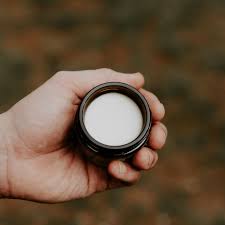 Hand holding an open jar of grooming balm