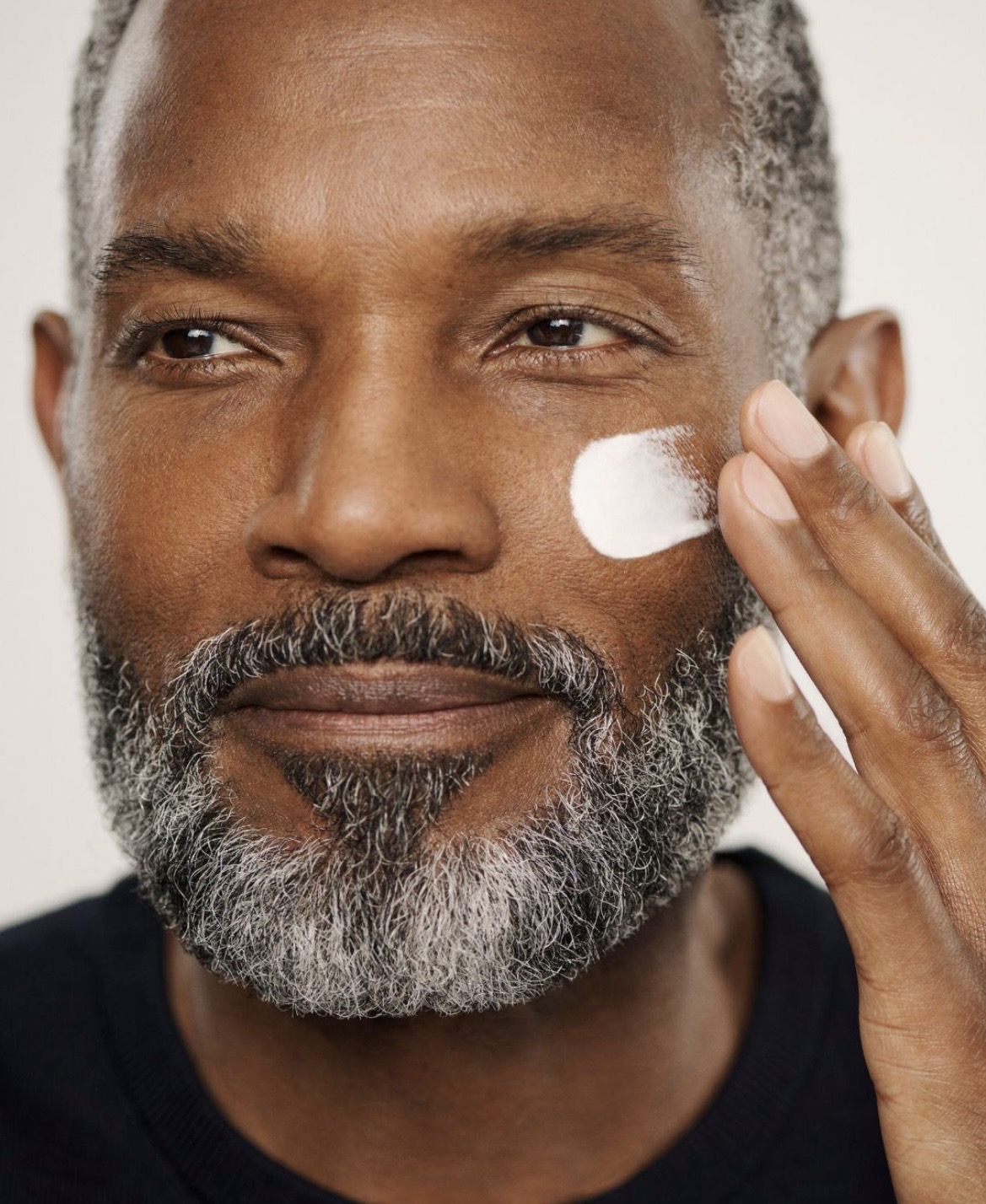Mature man applying moisturizer to his cheek